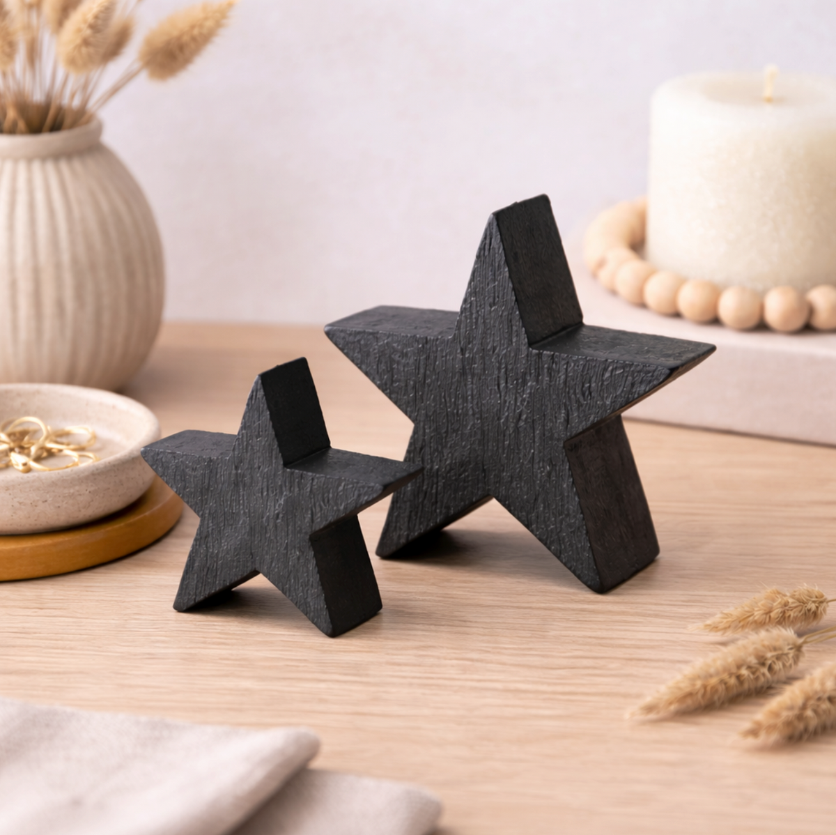 Black Mango Wood Star Ornament, Medium beside a smaller star on a table with candles