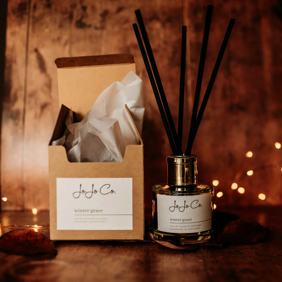 JoJo Co. Winter Grace Luxury Diffuser with black reeds, shown beside its kraft gift box in cosy lighting