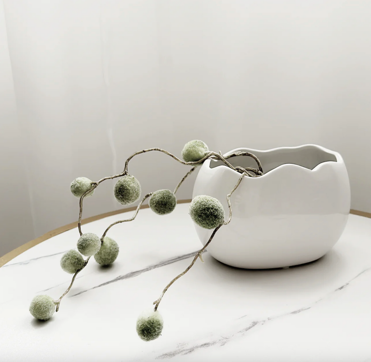 Napoli Dish, a white ceramic bowl with a wavy rim, on a marble table with trailing greenery
