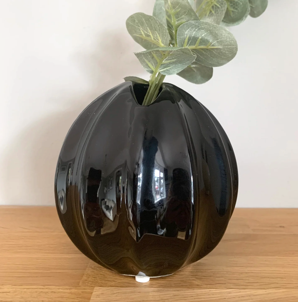 Nova Vase - Black Gloss, a round ribbed black vase holding eucalyptus, on a wooden surface