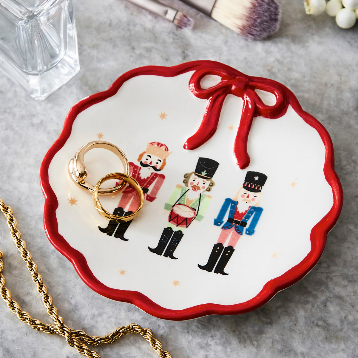 Nutcracker Trinket Dish With Bow holding rings, white scalloped dish with red bow and nutcrackers