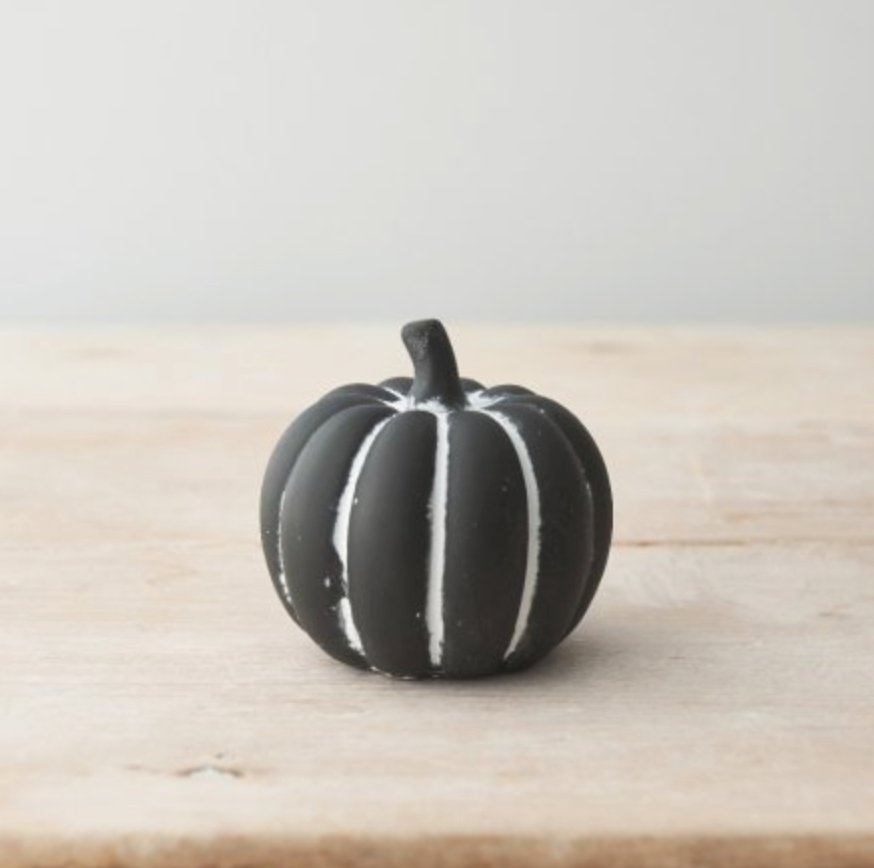 Black Cement Pumpkin Small, a black pumpkin with white ribs, on a plain pale wooden surface