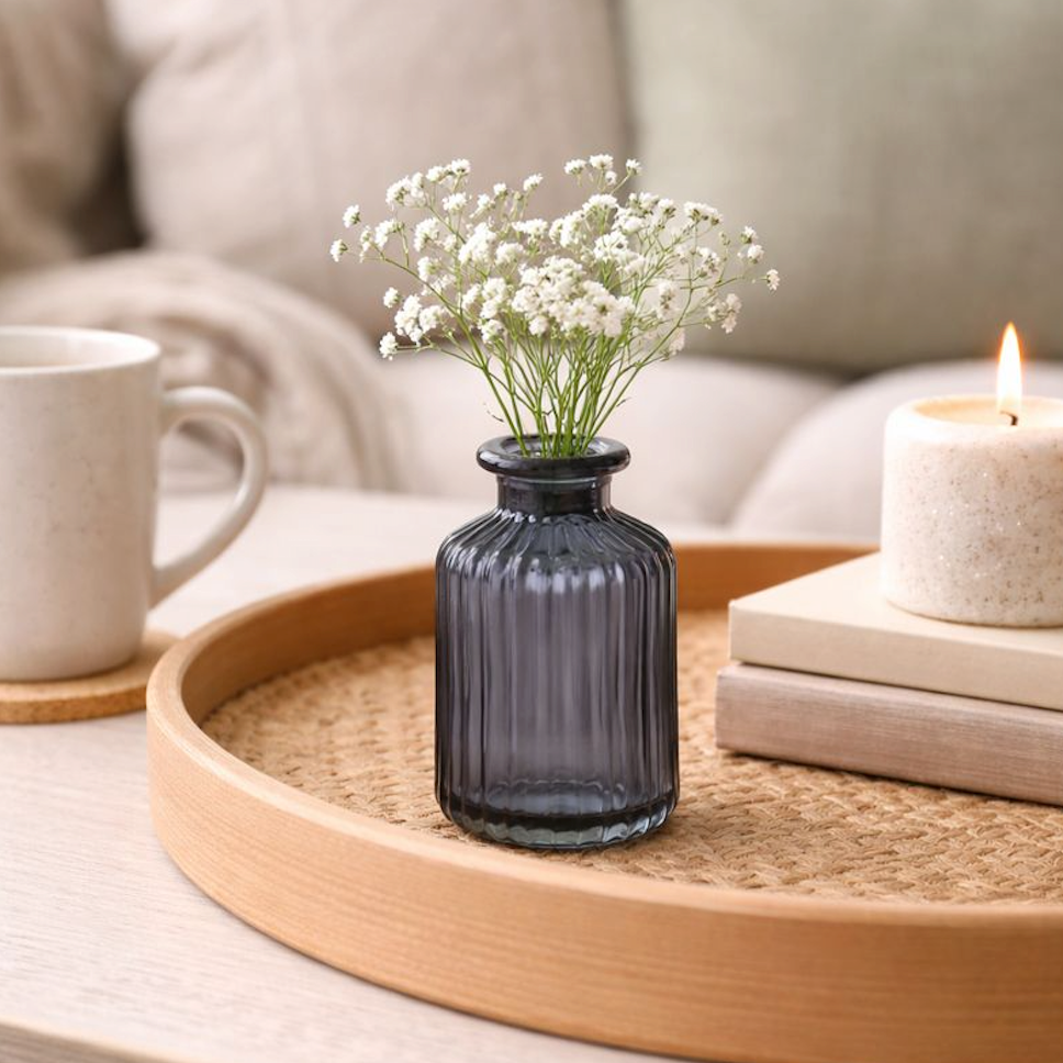 Blue Ribbed Glass Bottle Vase with a sprig of white gypsophila, on a round wooden tray by a candle