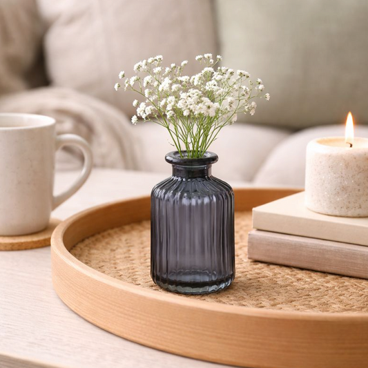 Blue Ribbed Glass Bottle Vase with a sprig of white gypsophila, on a round wooden tray by a candle