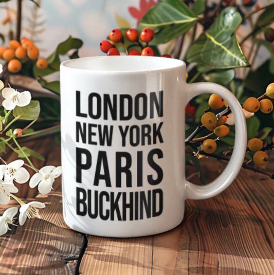 Buckhind Mug, a white mug with London New York Paris Buckhind text, on a wooden table with autumn berries