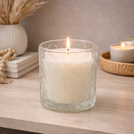 Devon Scent Diamond Cut Glass Candle, a lit cream candle in a clear faceted glass jar beside dried grasses