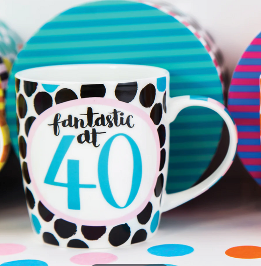Fantastic at 40 Mug, a white mug with black spots and a blue 40 badge, in front of a teal striped box