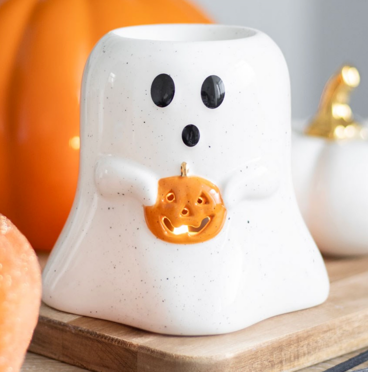 Ghost Shaped Wax/Oil Burner in white ceramic holding a small orange pumpkin, beside pumpkins
