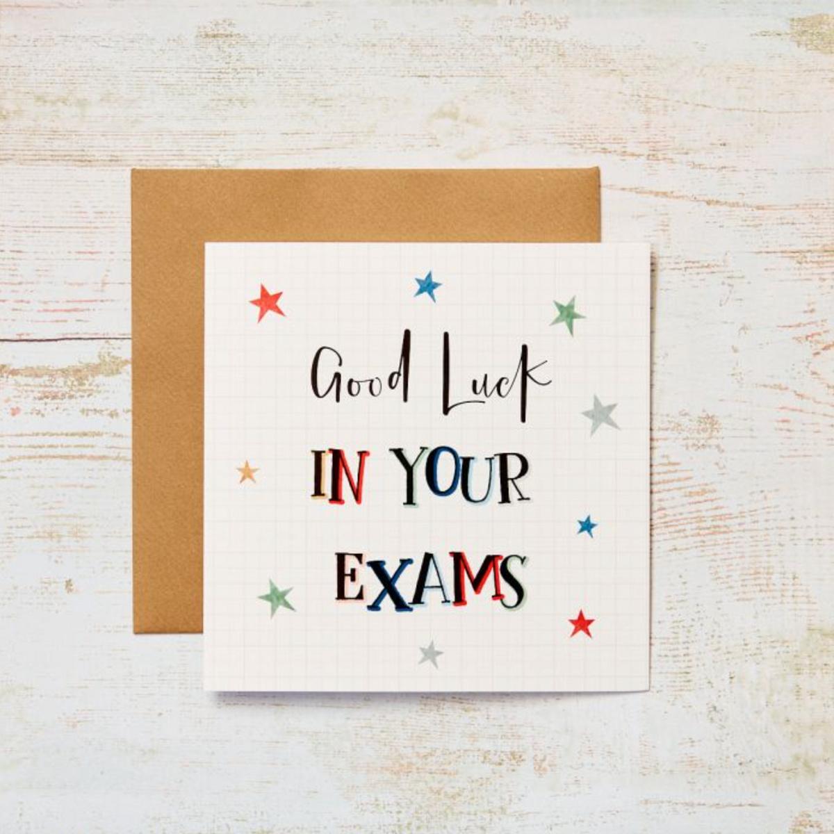 Good Luck in Your Exams Card with colourful mixed lettering and stars on white, with a kraft envelope