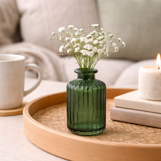 Green Ribbed Glass Vase holding white gypsophila on a round wooden tray beside a mug and candle