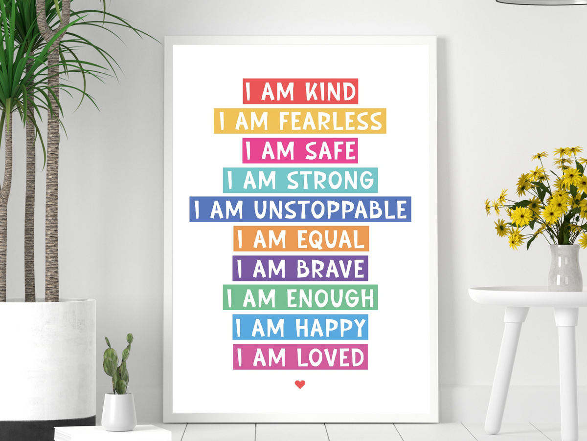 I Am Affirmation Colour print in a white frame on a pale wall beside yellow flowers and a plant