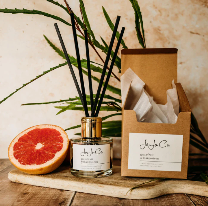 JoJo Co. Grapefruit & Mangosteen Luxury Diffuser with black reeds beside its kraft gift box and a halved grapefruit