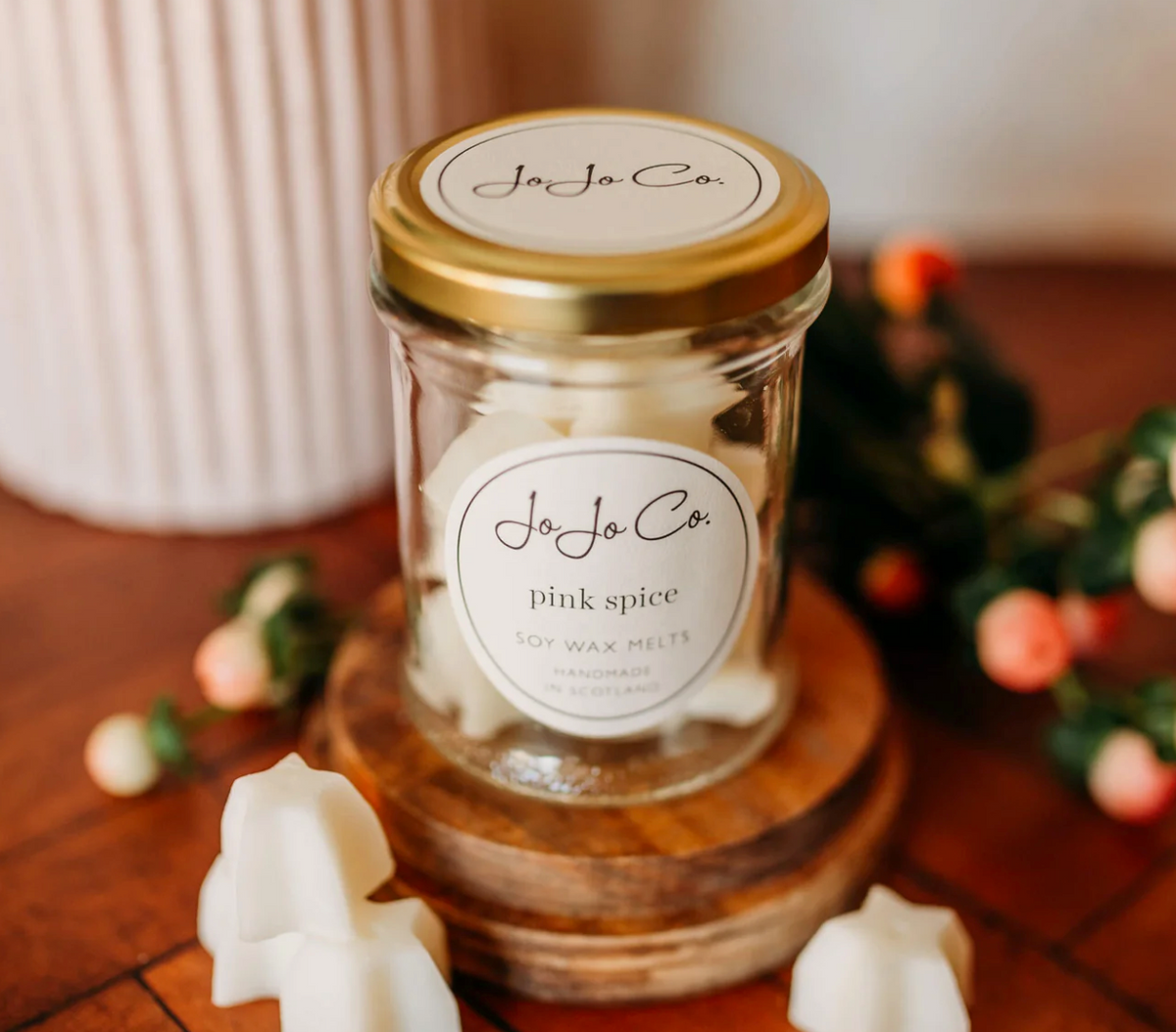 JoJo Co. Pink Spice Soy Luxury Wax Melts in a glass jar with white melts scattered on a wooden board