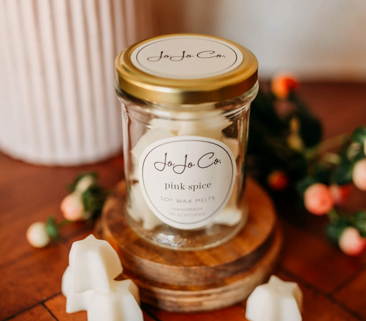 JoJo Co. Pink Spice Soy Luxury Wax Melts in a glass jar with white melts scattered on a wooden board