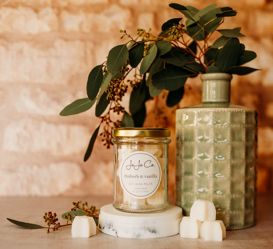 JoJo Co. Rhubarb & Vanilla Soy Luxury Wax Melts in a glass jar with melts, beside a vase of eucalyptus