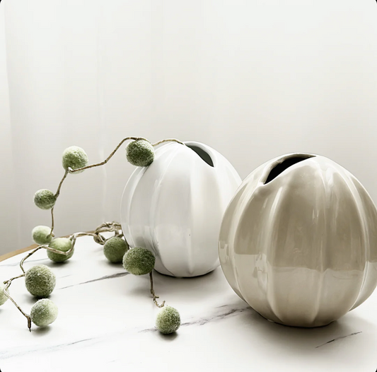 Nova Vase - Nude Gloss, a round ribbed vase in glossy nude, beside a white version with trailing greenery