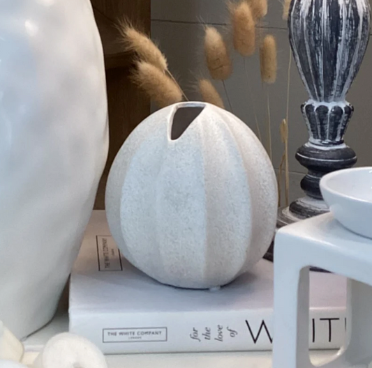 Nova Vase - Textured Effect, a round white ribbed vase with a speckled finish, on a stack of books