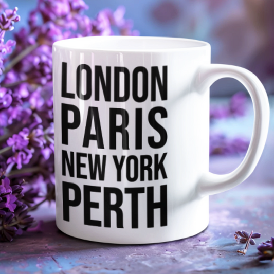 Perth Mug, a white mug with bold black London Paris New York Perth lettering, among purple lavender