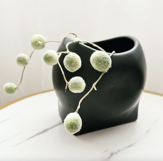 Poppy Vase - Black, a glossy black sculptural vase with an uneven rim and trailing greenery, on marble