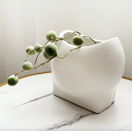 Poppy Vase - White, a matt white sculptural vase with a curved rim, holding trailing greenery on marble