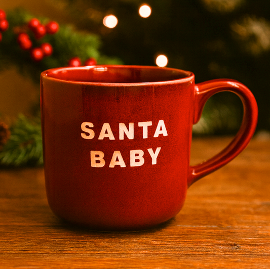 Santa Baby Mug in red with cream lettering on a wooden table with festive lights