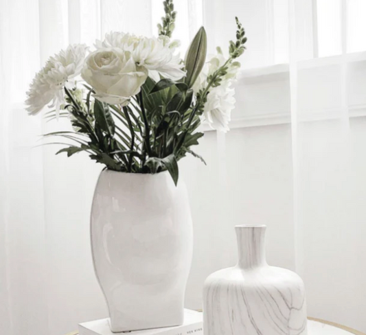 Soho Vase - Medium Gloss White, a curved white vase holding white flowers beside a smaller vase by a window