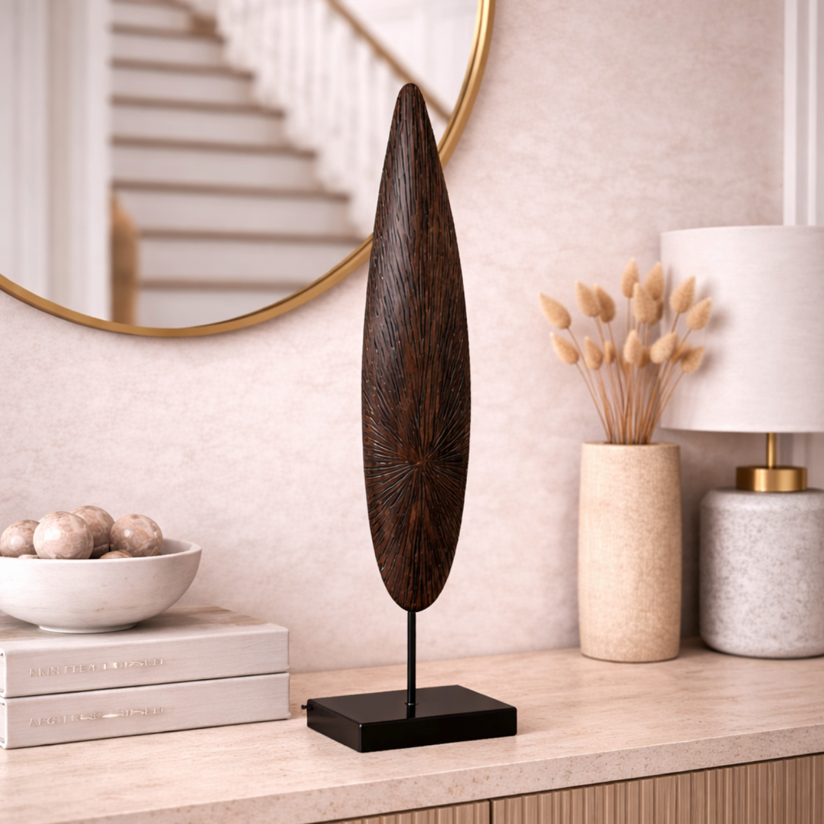 Solara Spire Sculpture, a tall dark wooden leaf-shaped spire on a black stand, displayed on a sideboard by a round mirror