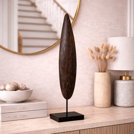 Solara Spire Sculpture, a tall dark wooden leaf-shaped spire on a black stand, displayed on a sideboard by a round mirror