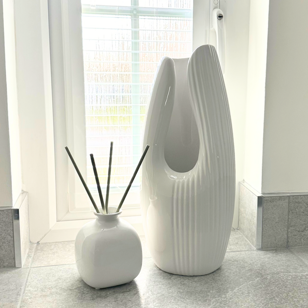 Tasha Vase (Various Colours) in white shown with a tall ribbed vase and reed diffuser by a window