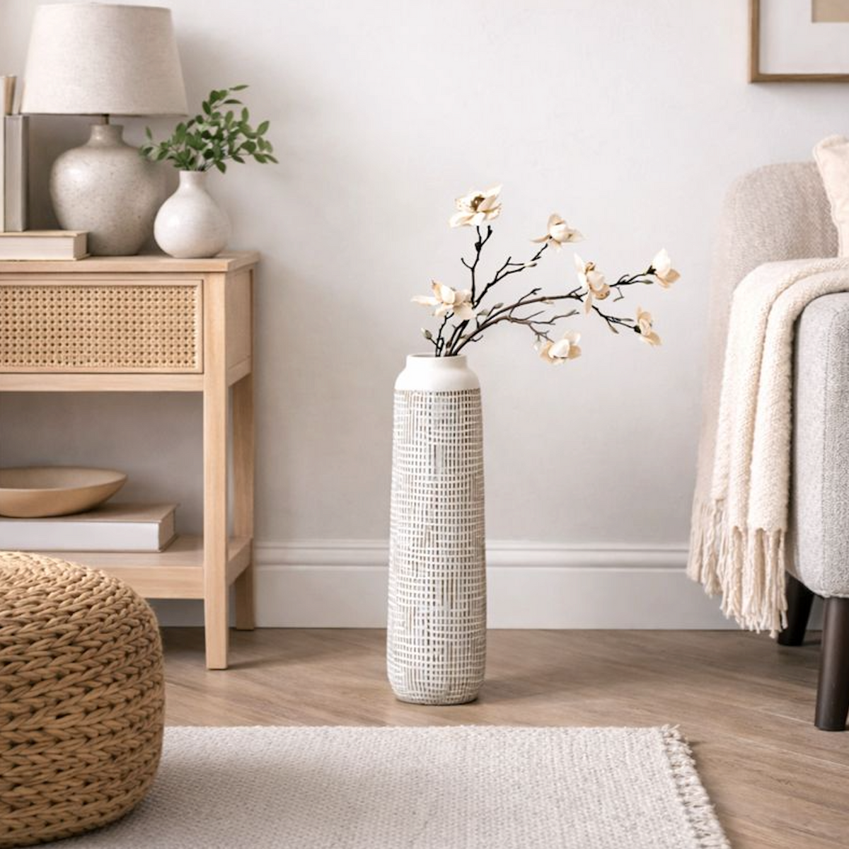 Textured Tall Polyresin Floor Vase, Large, holding blossom stems beside a rattan side table and armchair