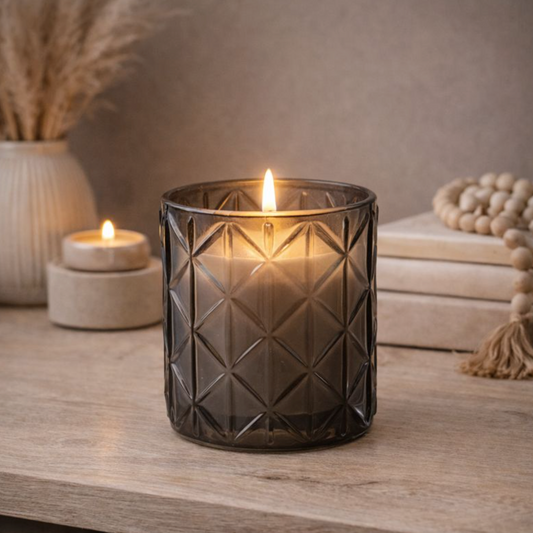 Woodsage & Sea Salt Smokey Black Diamond Glass Candle, lit in a faceted dark glass jar on a stone shelf